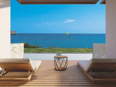 Strandzicht vanaf een houten terras met twee ligstoelen en een klein tafeltje onder een luifel.