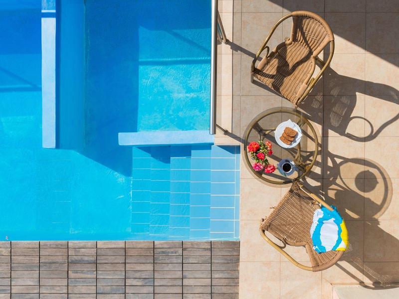 Bovenaanzicht van een helderblauw zwembad naast twee rieten stoelen en een tafel met drankjes en een globe.