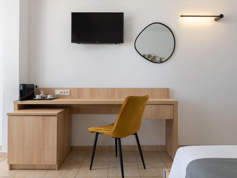 Minimalistisch bureau in hotelkamer met gele stoel, tv aan de muur, ronde spiegel en houten meubels.