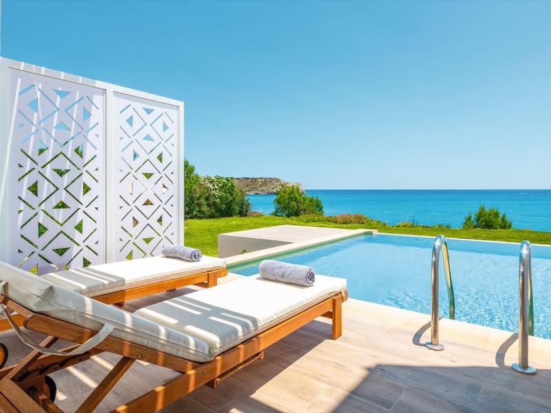 Ligstoelen bij het zwembad met handdoeken kijken uit op een blauw zwembad en heldere oceaan onder een zonnige hemel.