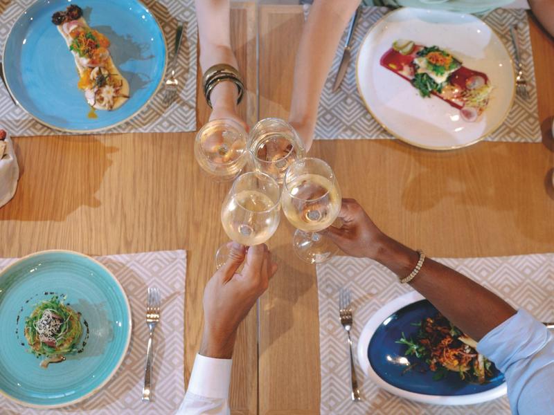 Vier personen proosten met wijnglazen aan een tafel met verfijnde gerechten op kleurrijke borden.