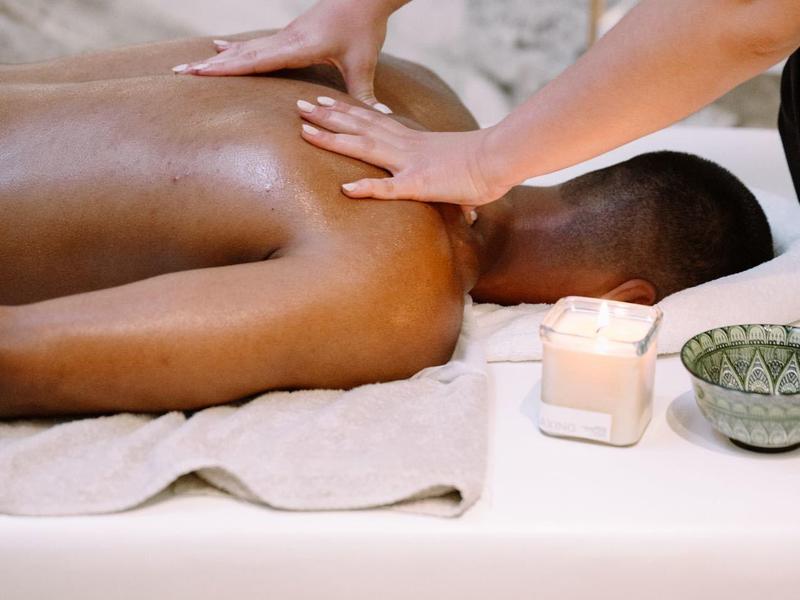 Persoon krijgt een rugmassage op een wit tafelblad met kaars en kom in de buurt.