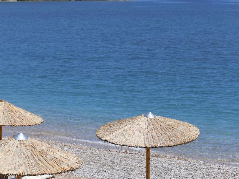 Strand met twee ligstoelen en parasols op een kiezelstrand, rustige blauwe zee op de achtergrond.