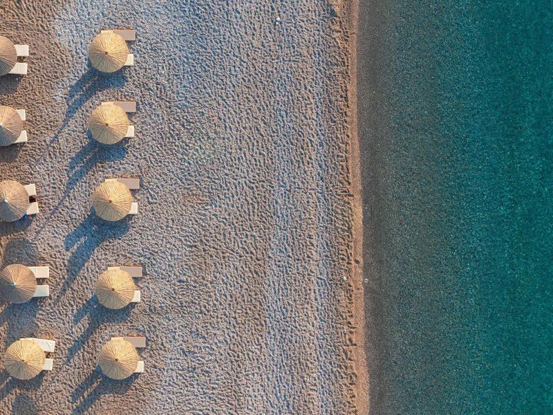 Luchtfoto van een kiezelstrand met parasols naast helderblauw water.