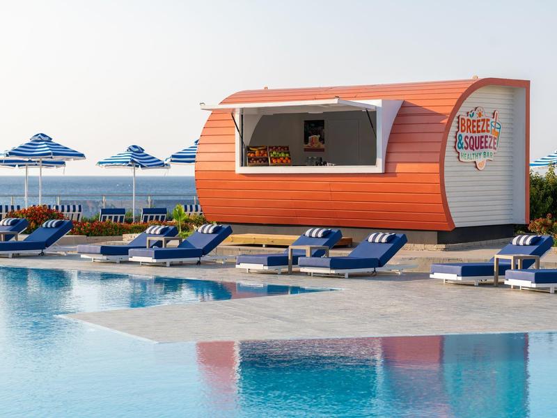 Moderne oranje foodtruck naast zwembad met blauwe ligstoelen en parasols aan zee.