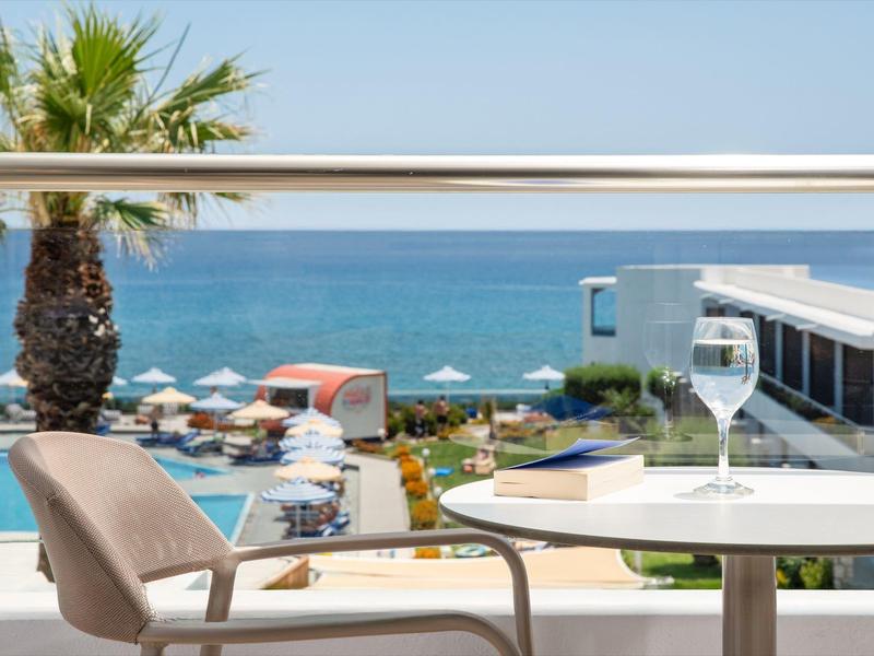Balkon met tafel, stoel en uitzicht op zee boven een zwembad en palmbomen.