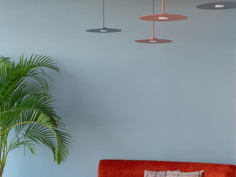 Modern interieur met rode bank, kussen, hanglampen en een potplant.