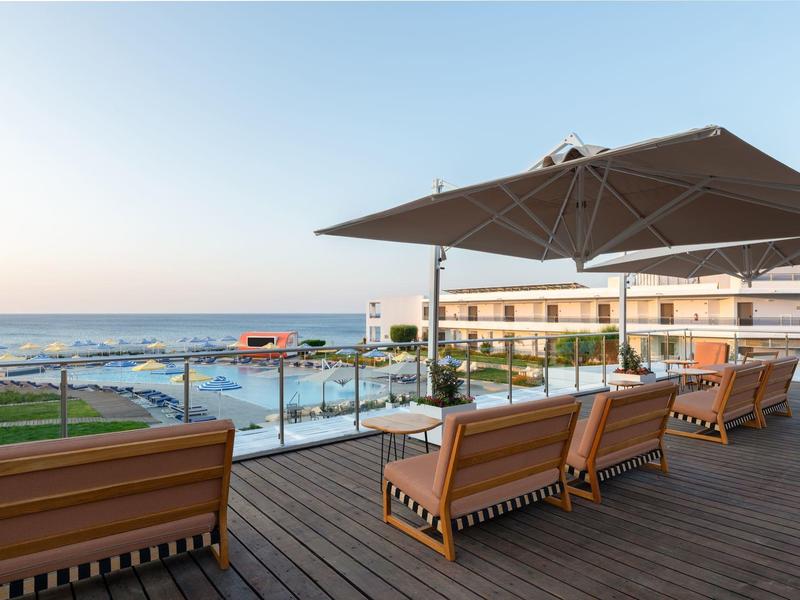 Terras met houten vloer, zitplaatsen en grote parasol met uitzicht op zee.