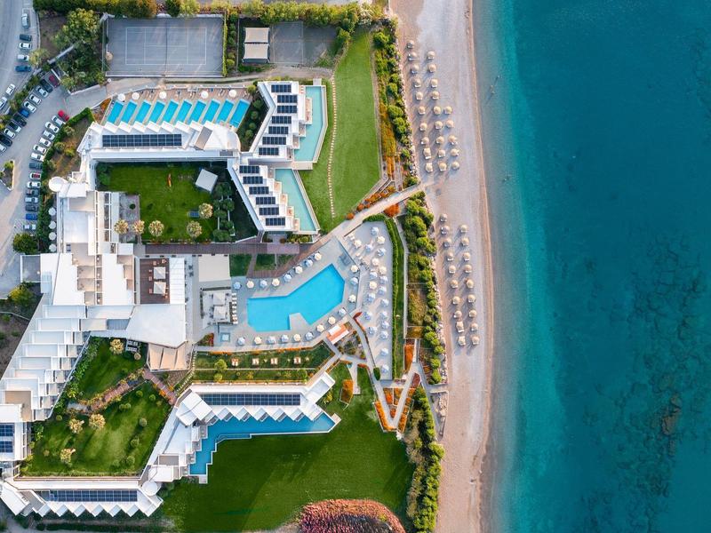 Luchtfoto van een hotel met meerdere zwembaden direct aan helderblauwe zee en zandstrand.