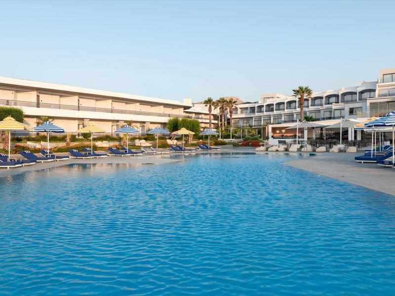 Groot buitenzwembad omringd door ligstoelen en parasols naast een modern hotelgebouw.