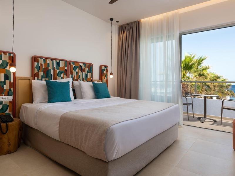 Modern hotelkamer met tweepersoonsbed, artistiek hoofdeinde en zeezicht.