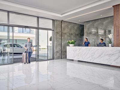 Reception dell'hotel con due addetti dietro un banco in marmo e un ospite con bagaglio.