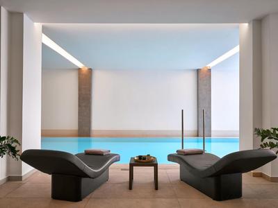 Piscina interna moderna con due lettini e un piccolo tavolo in un ambiente elegante.