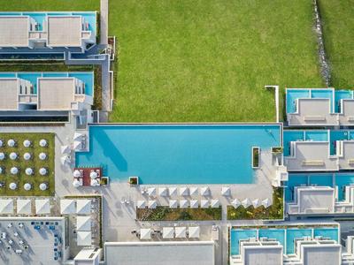 Widok z lotu ptaka nowoczesnego hotelu z długim niebieskim basenem i zielonym trawnikiem.