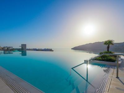 Basen typu infinity z widokiem na morze o zachodzie słońca z palmami przy basenie