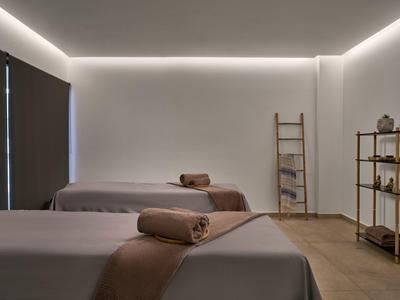 Stanza benessere minimalista con due lettini, illuminazione soffusa e scaffali decorativi.