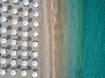 Veduta aerea di una spiaggia con ombrelloni, sabbia e acqua azzurra limpida.