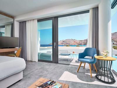 Camera d'hotel moderna con grandi finestre, area salotto e vista sulle montagne alla luce del sole.