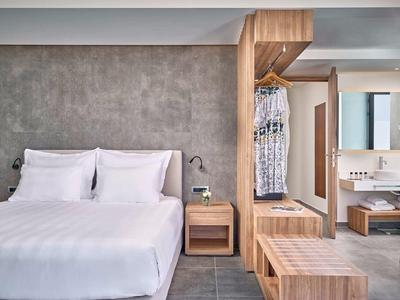 Camera d'hotel moderna e accogliente con letto matrimoniale, comodino e guardaroba aperto in tonalità neutre.