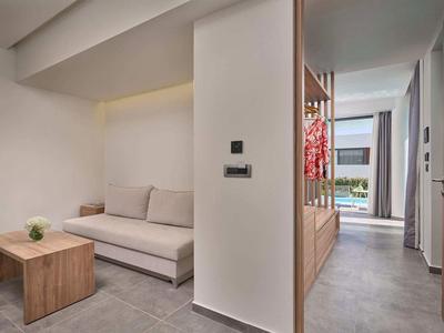 Camera d'hotel moderna con divano, tavolo in legno e vista sulla piscina attraverso le finestre.