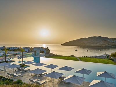 Tramonto su una terrazza con piscina con ombrelloni bianchi e vista sul mare.