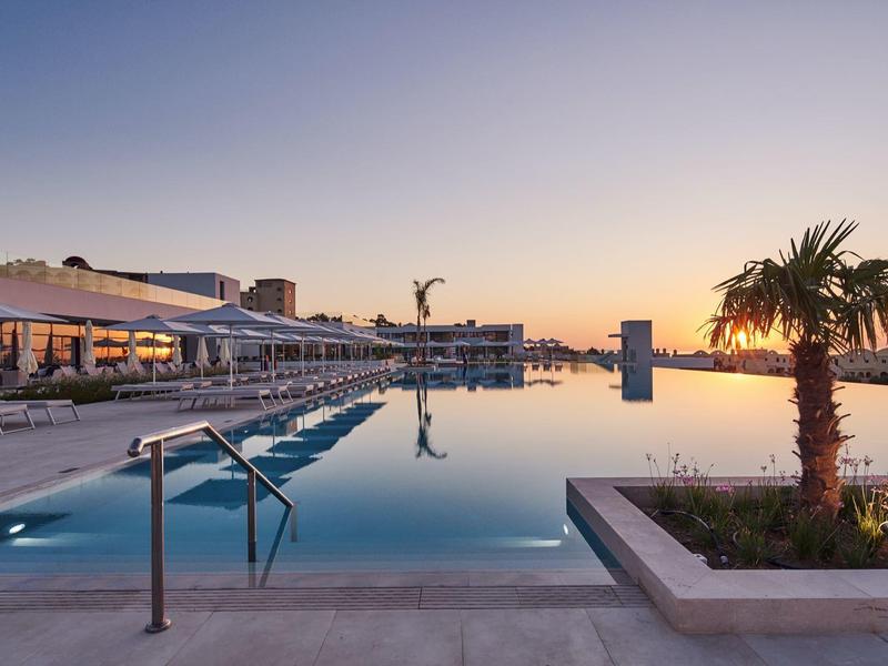 Piscina a sfioro in un hotel con vista sul tramonto e palme.