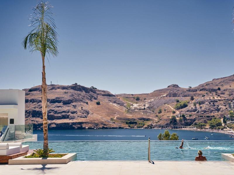 Piscina a sfioro con vista su lago calmo e colline aride sotto cielo limpido.