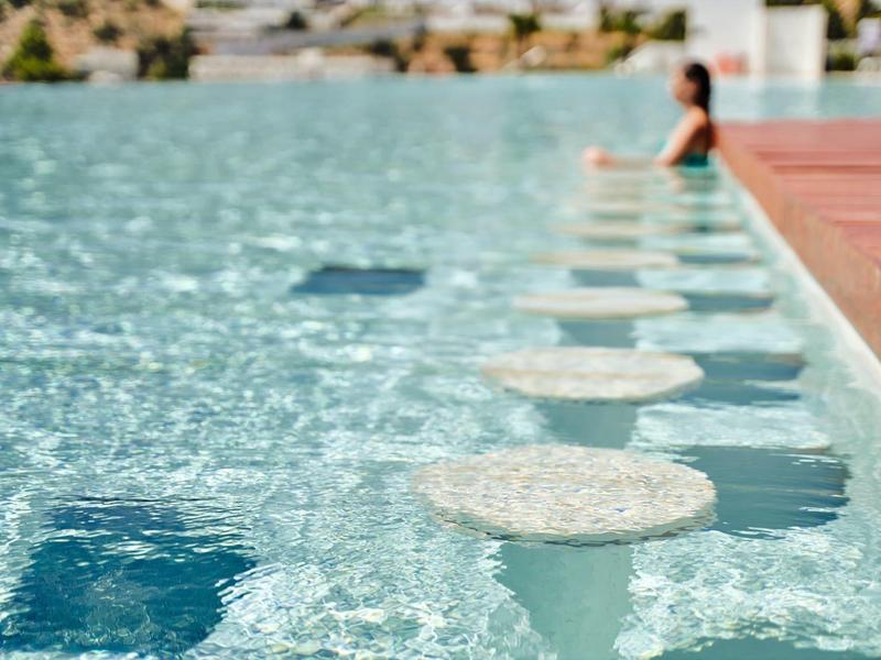 Piscina con sgabelli rotondi integrati e una persona sul bordo.