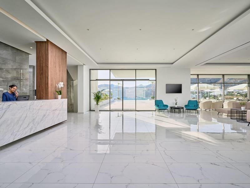 Luminoso ingresso d'hotel moderno con pavimento in marmo lucido, reception e area salotto con vista.
