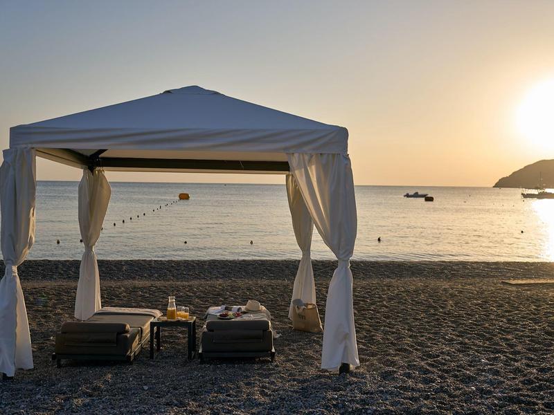 Due chaise lounge sotto un baldacchino bianco sulla spiaggia al tramonto.