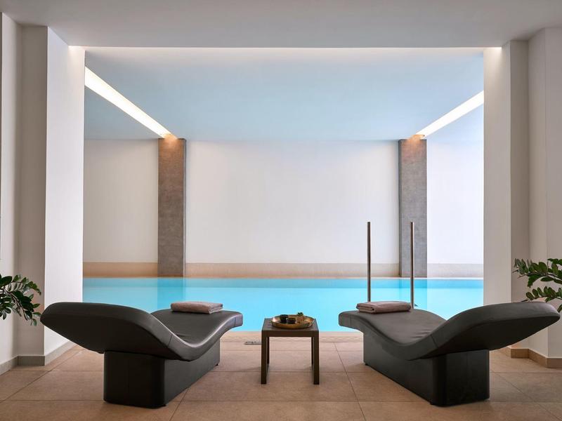 Piscina interna moderna con due lettini e un piccolo tavolo in un ambiente elegante.