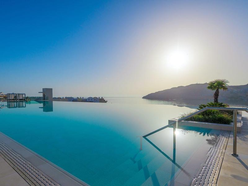 Piscina a sfioro con vista sul mare e sulle montagne al tramonto.