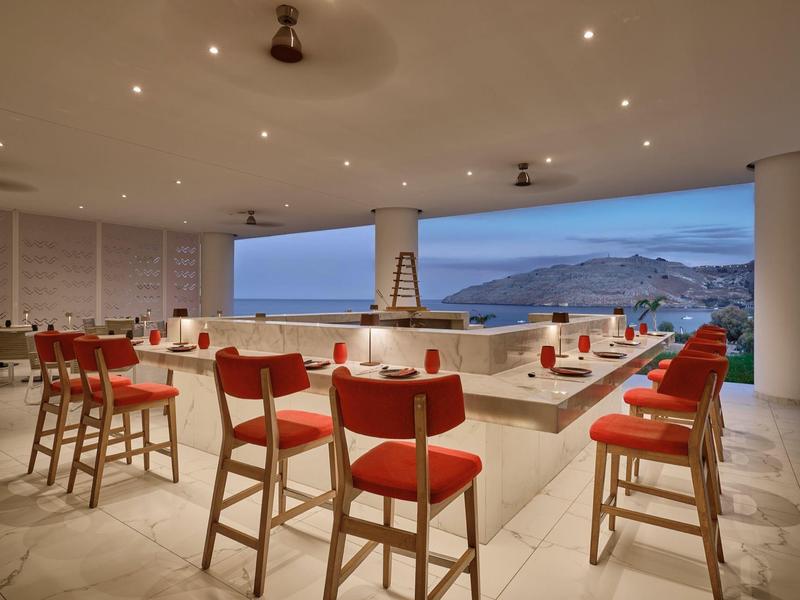 Area bar moderna e aperta con sedie rosse con vista sul mare al tramonto.