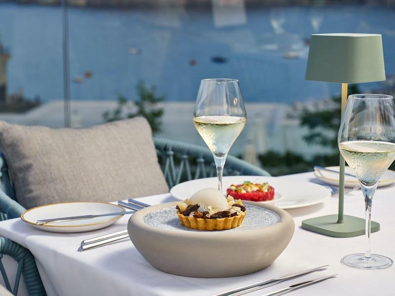 Tavolo elegante apparecchiato con vino, dessert e lampada su terrazza vista mare