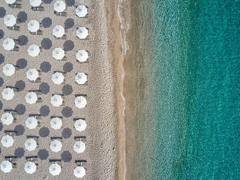 Veduta aerea di una spiaggia con ombrelloni, sabbia e acqua azzurra limpida.