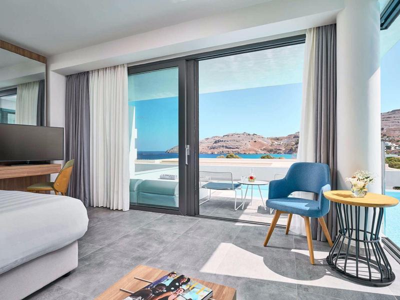 Camera d'hotel moderna con grandi finestre, area salotto e vista sulle montagne alla luce del sole.