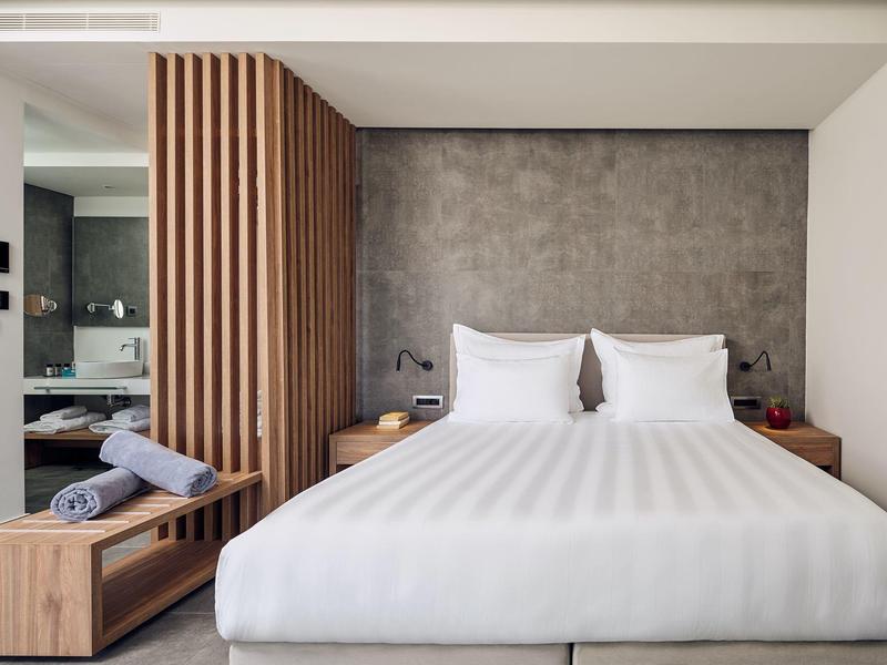 Camera d'hotel moderna con letto matrimoniale, dettagli in legno e parete grigia.