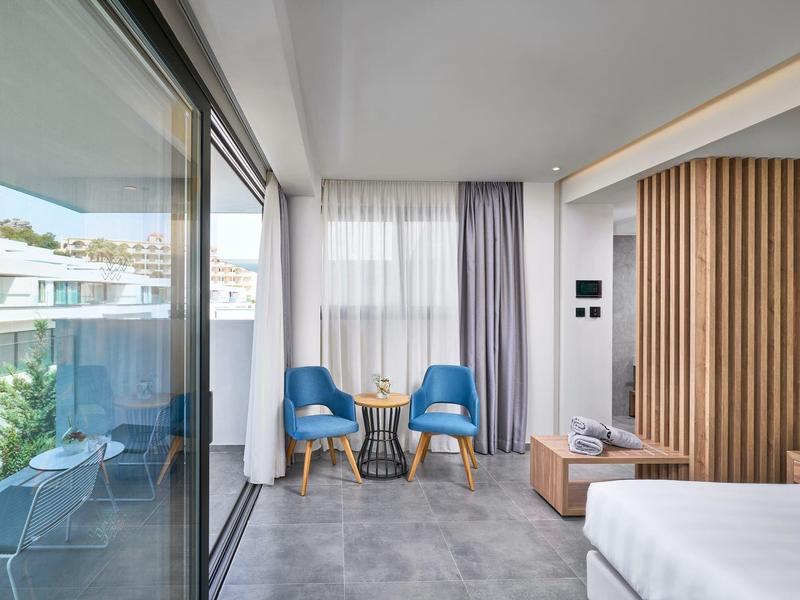 Camera d'hotel moderna con balcone, due poltrone blu e luce naturale.