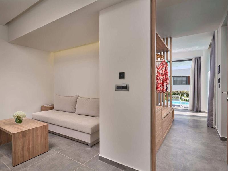 Camera d'hotel moderna con divano, tavolo in legno e vista sulla piscina attraverso le finestre.