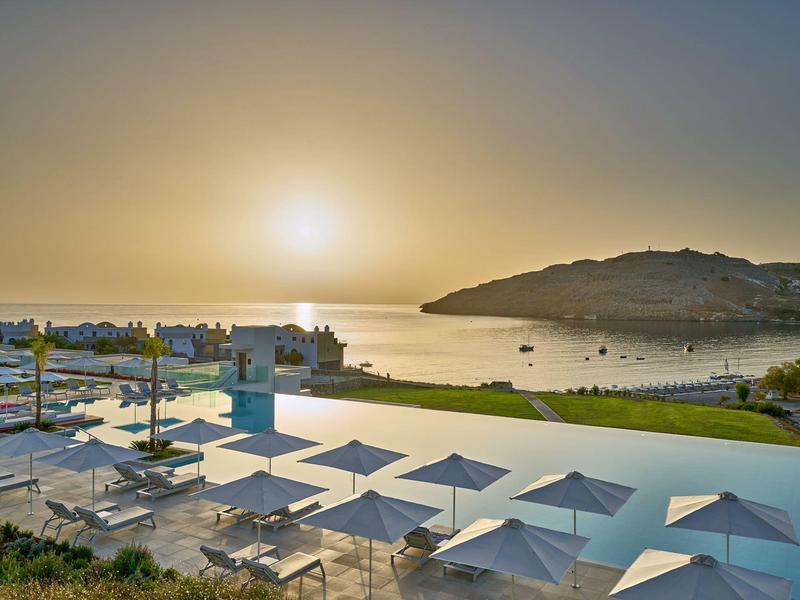 Tramonto su una terrazza con piscina con ombrelloni bianchi e vista sul mare.