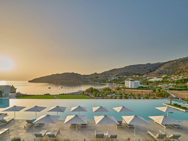 Piscina a sfioro con ombrelloni, lettini e vista sulle colline al tramonto.