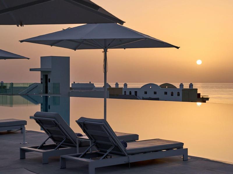 Due sdraio sotto ombrelloni accanto a una piscina tranquilla al tramonto.