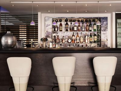 Área moderna de bar de hotel con taburetes blancos frente a una barra bien surtida.