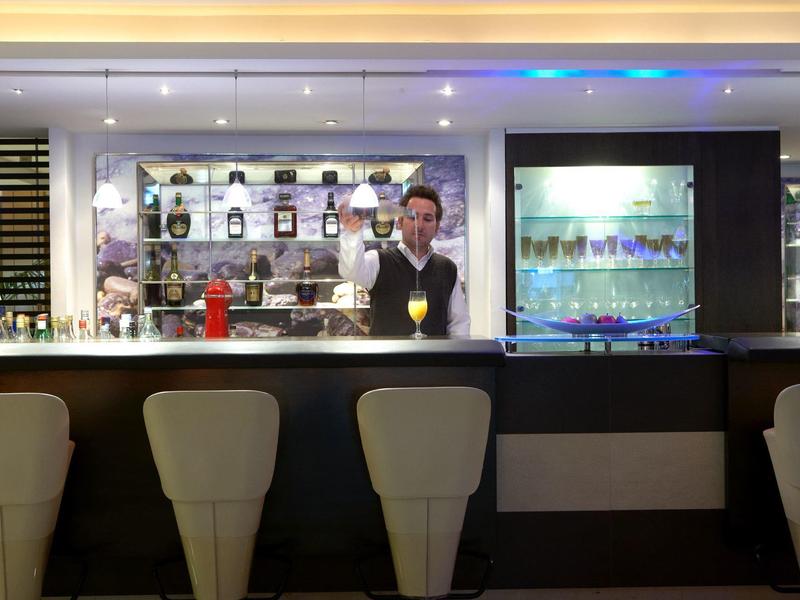 Moderne Bar mit fünf weißen Stühlen, Barkeeper und beleuchteten Regalen im Hintergrund.