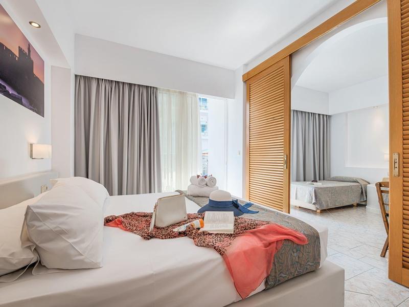 Hell eingerichtetes Schlafzimmer mit großen Fenstern, weißen Wänden, Holzschrank und gemütlichem Bett.