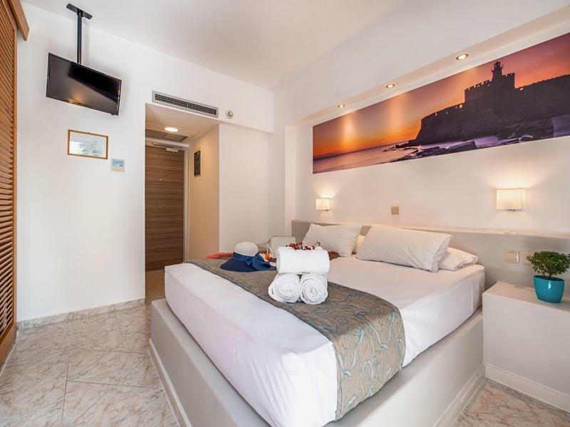 Helles Schlafzimmer mit großem Bett, Wandbild, TV und Nachttischen mit Pflanzen und Lampen.