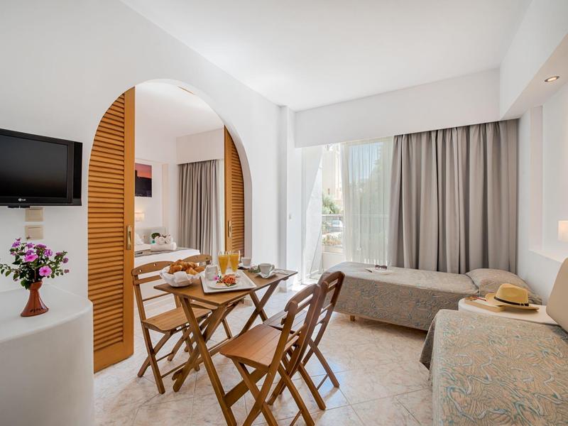 Heller Wohnraum mit Holztisch, Klappstühlen, zwei Sofas und großem Fenster mit Vorhängen.