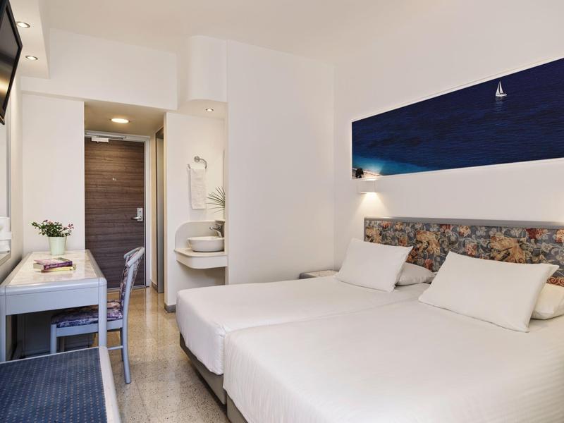 Modernes, helles Schlafzimmer mit zwei Betten, Schreibtisch, Stuhl und schlichter Dekoration.