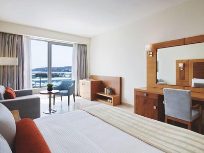 Habitación de hotel luminosa con cama, escritorio, sofá y balcón con vista al mar.