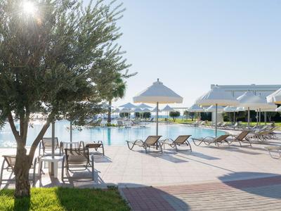 Sonniger Poolbereich mit Liegestühlen und Sonnenschirmen neben einem Hotelgebäude.
